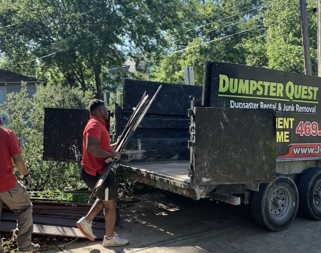 Two Dumpster Quest crew members loading metal rods into a dump trailer
