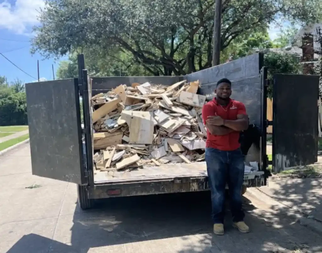 Dumpster Quest team member standing beside a dump trailer full of wood and drywall debris